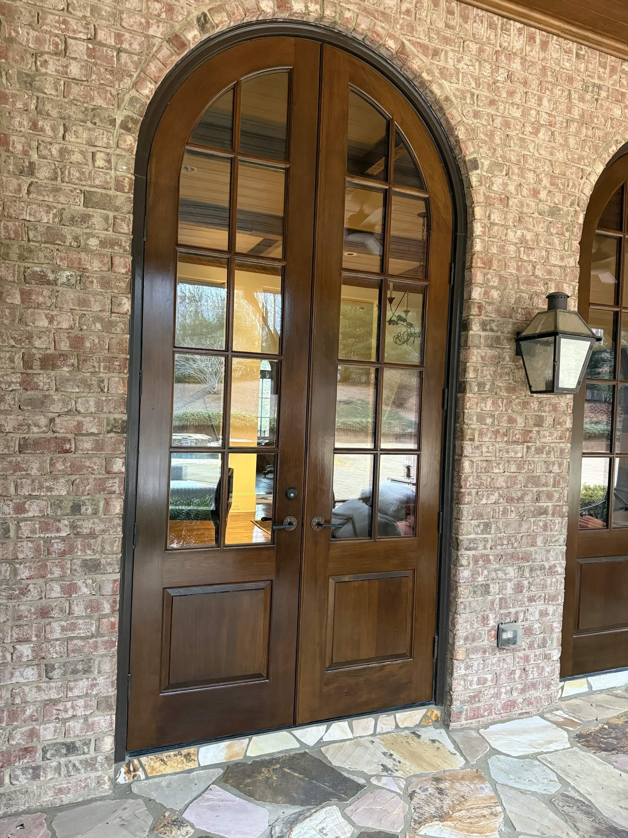 Arched wood-and-glass double front doors set into brick with a flagstone porch