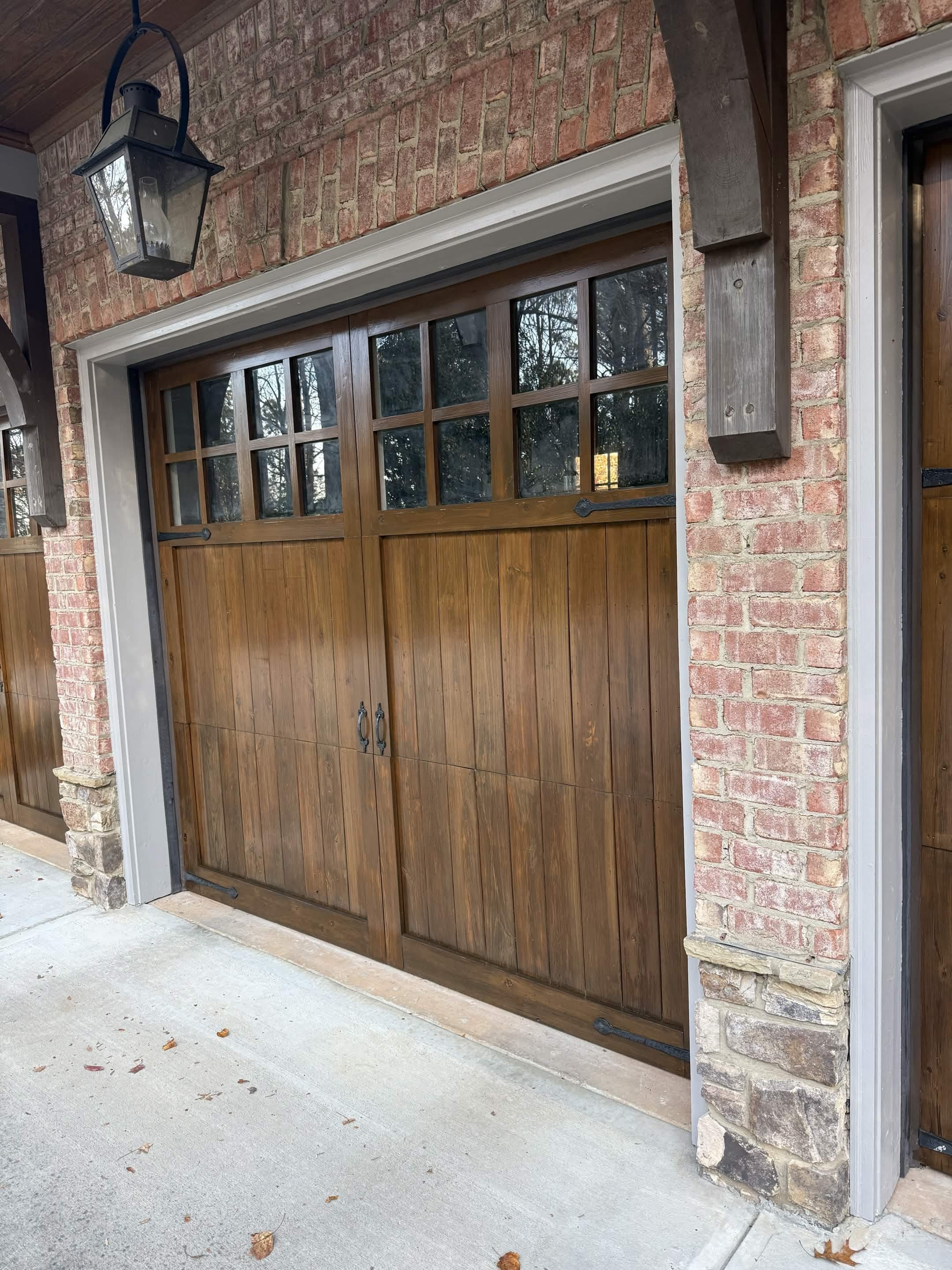 Custom wood carriage-style garage doors set into brick with a gas lantern