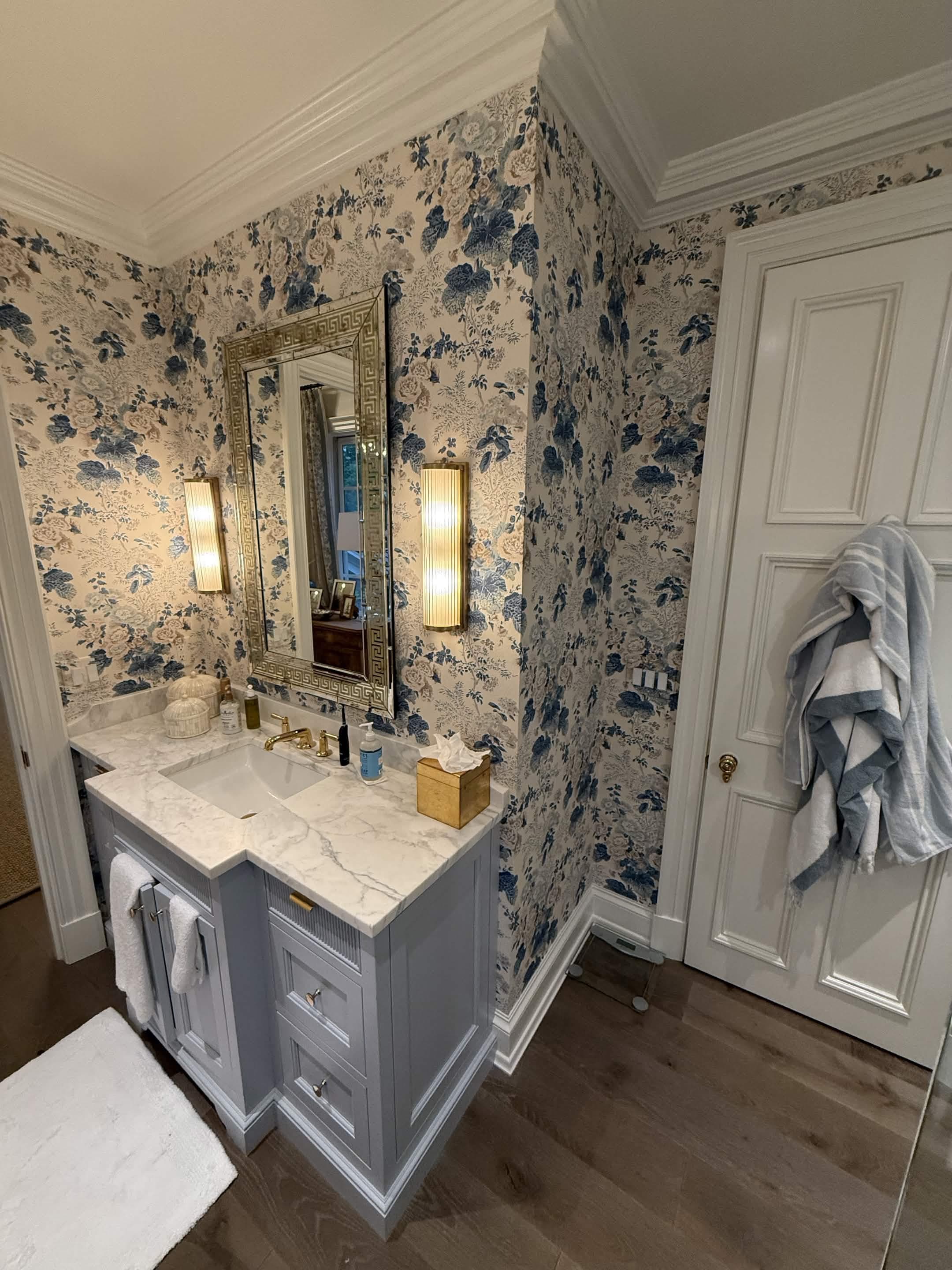 A dressing vanity with a marble top, silver-leaf mirror, and blue floral wallpaper