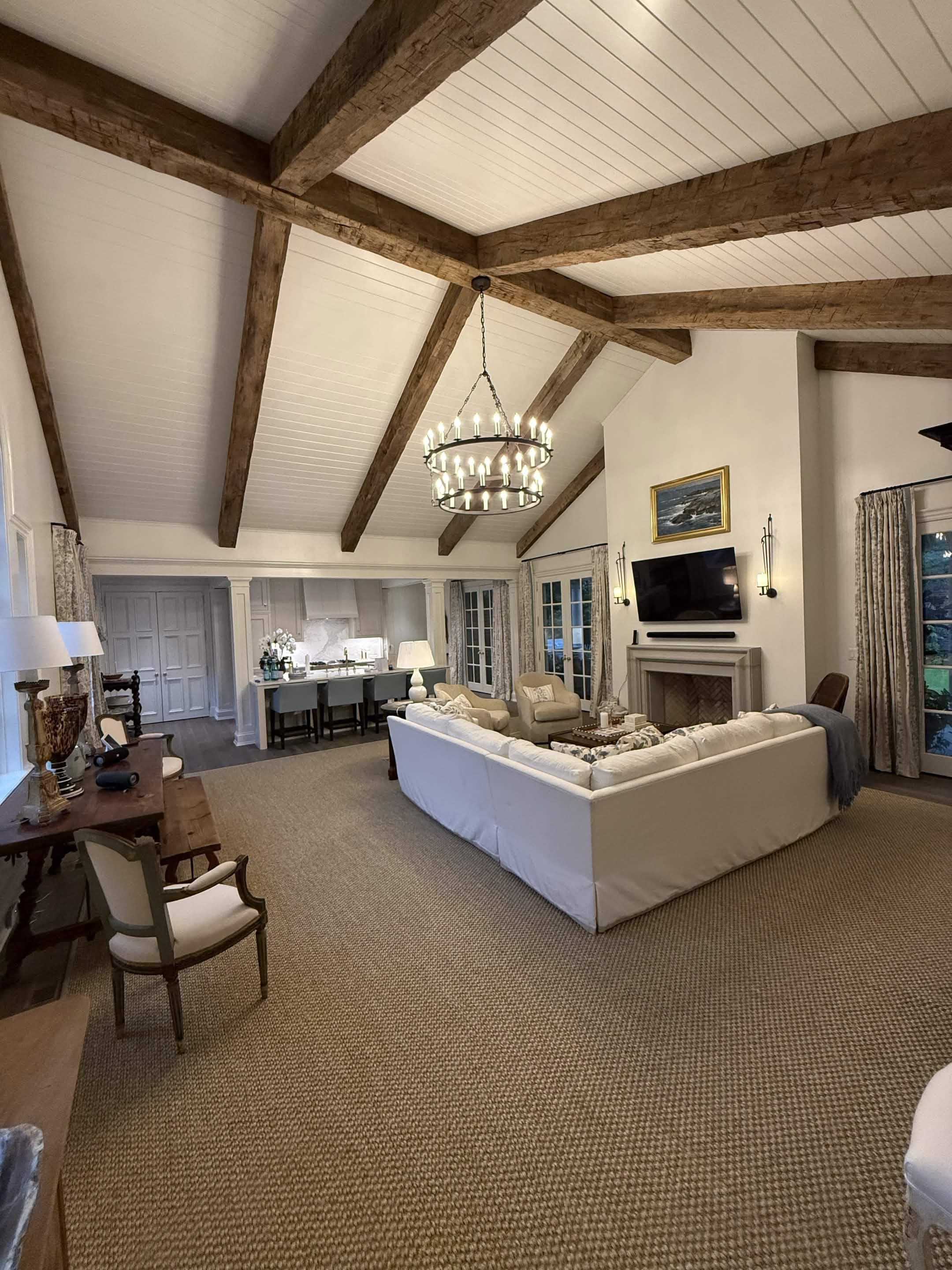 An open living hall under a beamed cathedral ceiling, opening to the kitchen beyond